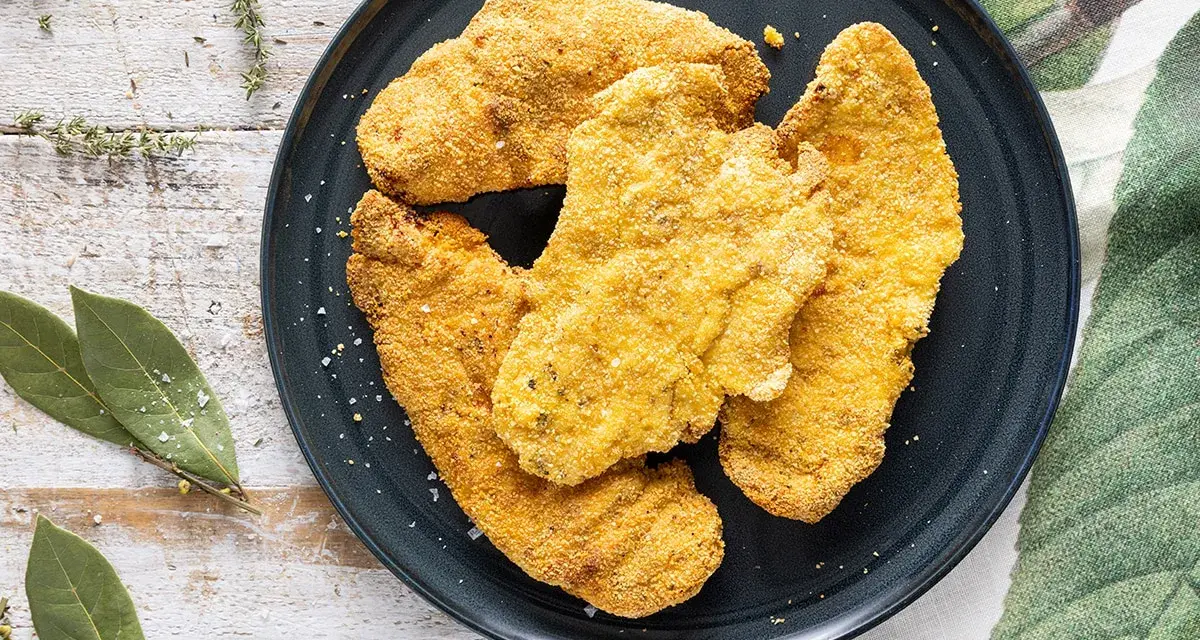 Cotolette dorate e croccanti, perfette cotolette in friggitrice ad aria, servite su un piatto scuro con erbe aromatiche e foglie di alloro.