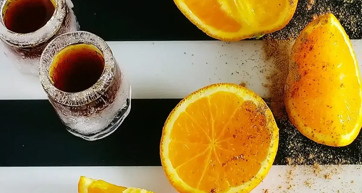 Dwa kieliszki z Jägermeisterem ze spritem, obok pokrojone pomarańcze posypane przyprawami.