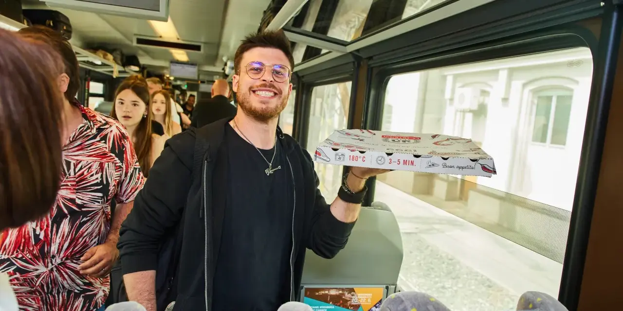 Uśmiechnięty mężczyzna z pizzą w ręku w pociągu relacji Kraków-Praga.