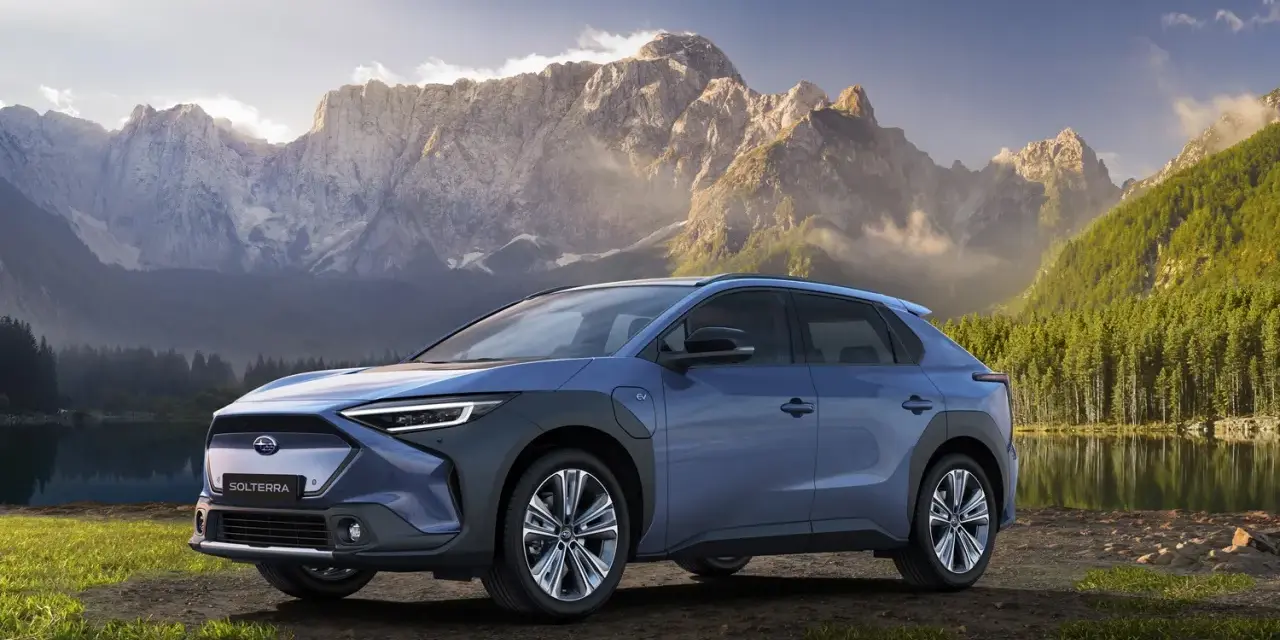 Niebieski Subaru Solterra stoi nad jeziorem z górami w tle.