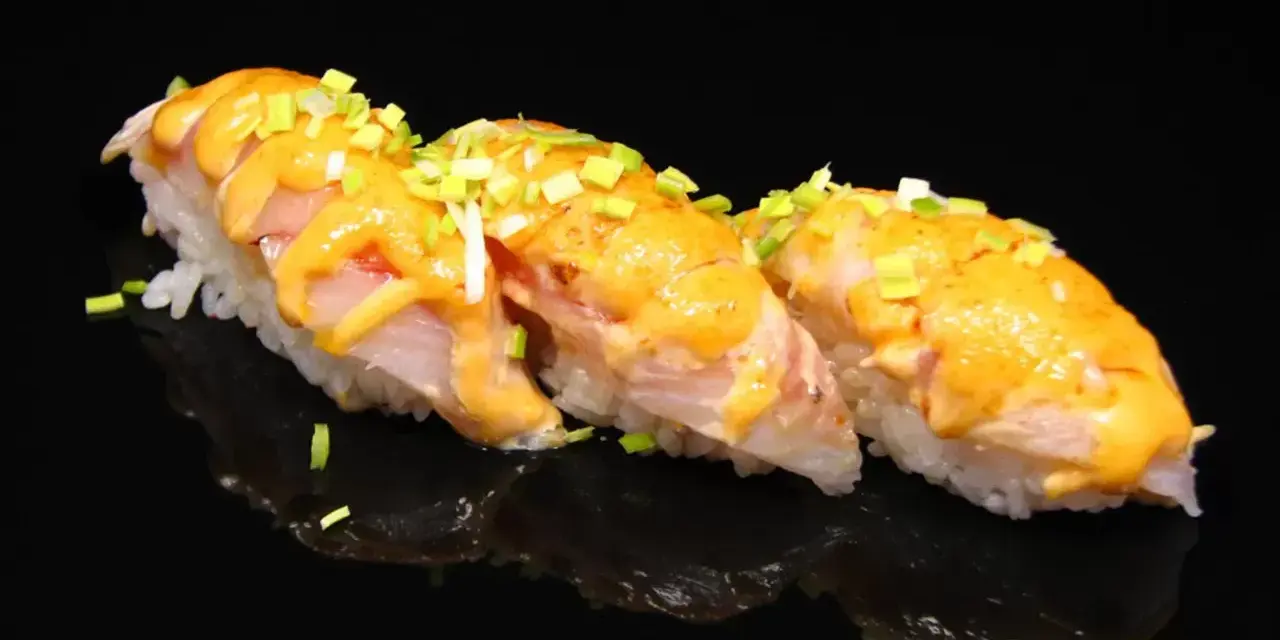 Trzy kawałki sushi z rybą i kremowym sosem, posypane szczypiorkiem. Idealne na lekki posiłek, gdy zastanawiasz się nad sushi kalorie.
