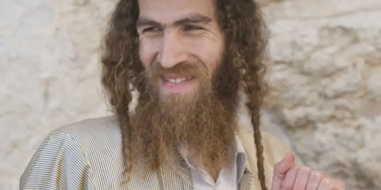 A smiling man with long, curly hair and a beard, wearing traditional Jewish attire. His appearance sparks curiosity about what ethnicity was Jesus.