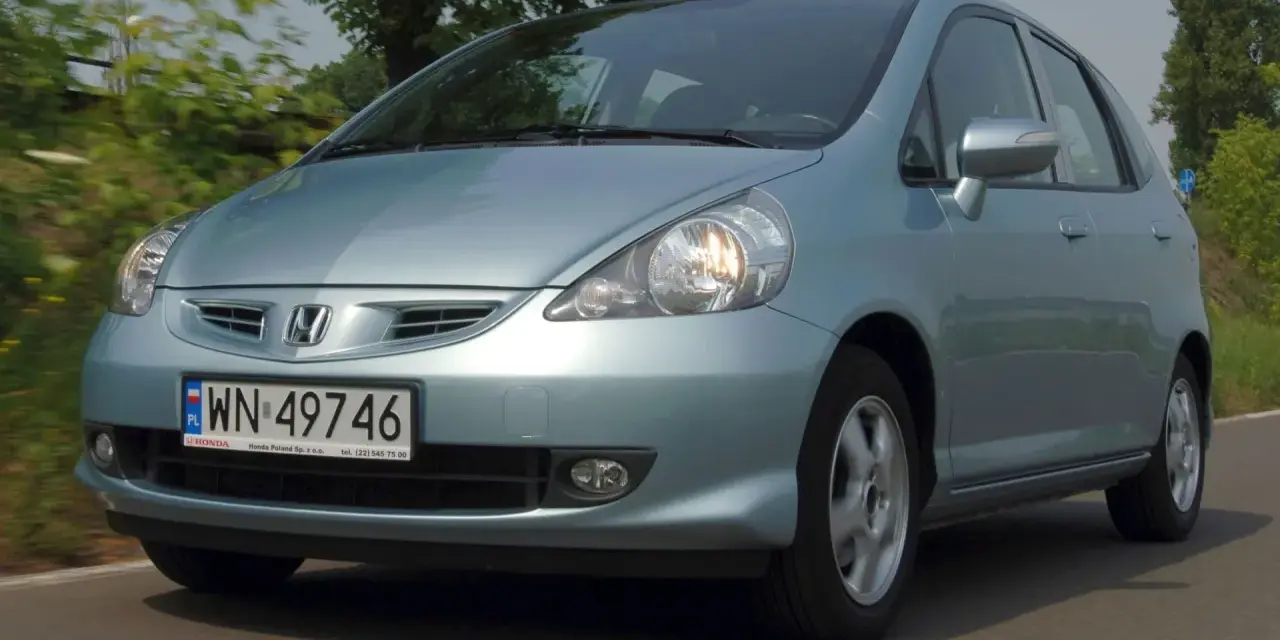 Jasnoniebieski Honda Jazz 2 na drodze, z zielenią w tle.