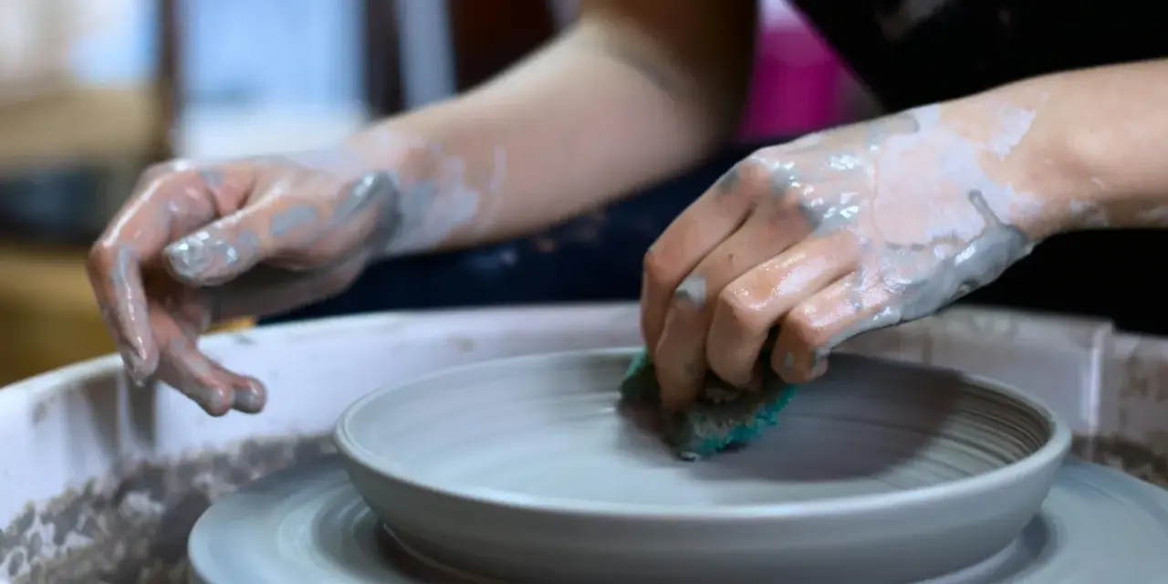Mani sporche di argilla lavorano su un piatto al tornio, creando forme uniche con lavori con argilla senza cottura.