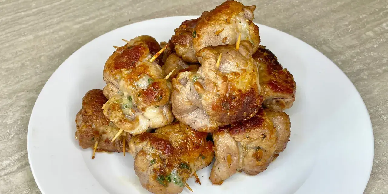 Un mucchio di bombette pugliesi ricetta, dorate e succulente, tenute insieme da stuzzicadenti, su un piatto bianco.