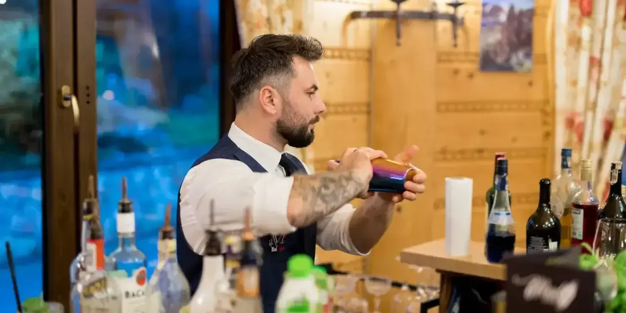 Barman na wesele cena: profesjonalista miesza drinki za barem, otoczony butelkami alkoholu i dekoracjami.