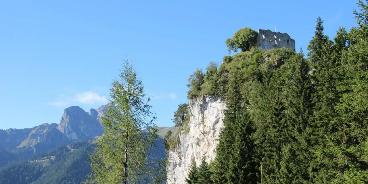 Burgruine Falkenstein thront auf Felsklippe, umgeben von Nadelbäumen. Perfekt für eine Wanderung mit Bergblick.