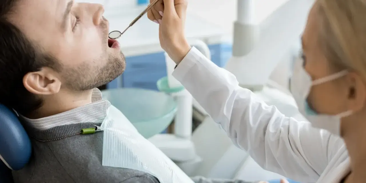 Pacjent u dentysty, zastanawia się, ile kosztuje wizyta u dentysty prywatnie. Lekarz bada jego zęby.