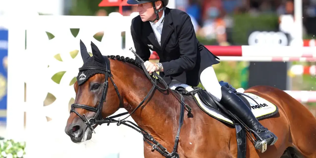 Cavalier en tenue d'équitation, sur un cheval bai, en plein saut. Le cheval, nommé Ratina Z, est concentré.