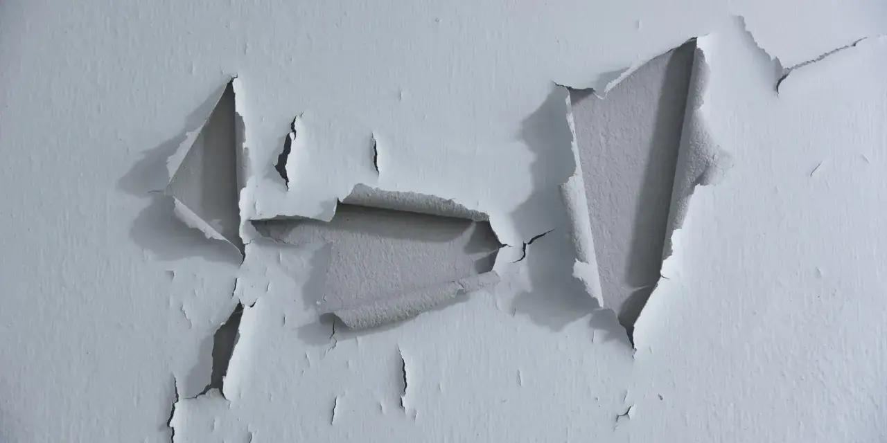 Pintura desconchada revela capas de color gris bajo la superficie blanca.