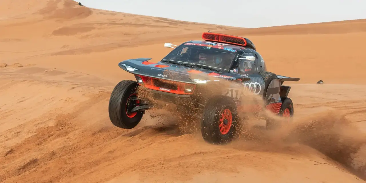 Un'auto da rally Audi sfreccia tra le dune, sollevando sabbia. Un'emozionante tappa del percorso Parigi-Dakar.
