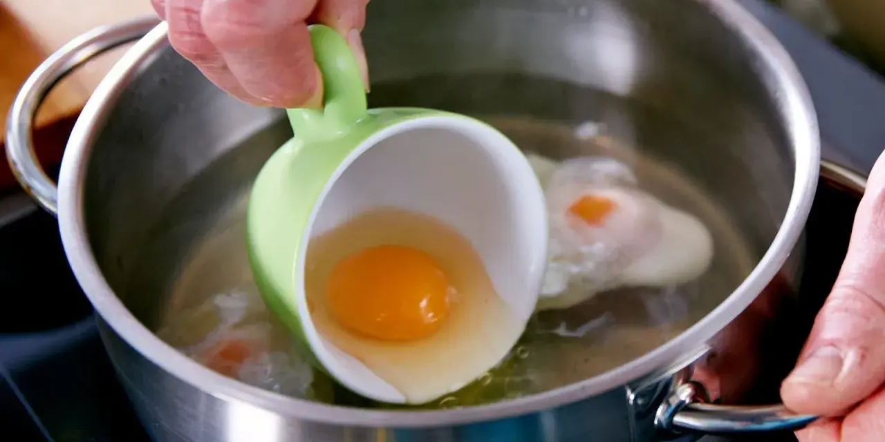Ein rohes Ei wird aus einer grünen Tasse in kochendes Wasser gegossen, um verlorene Eier zuzubereiten.