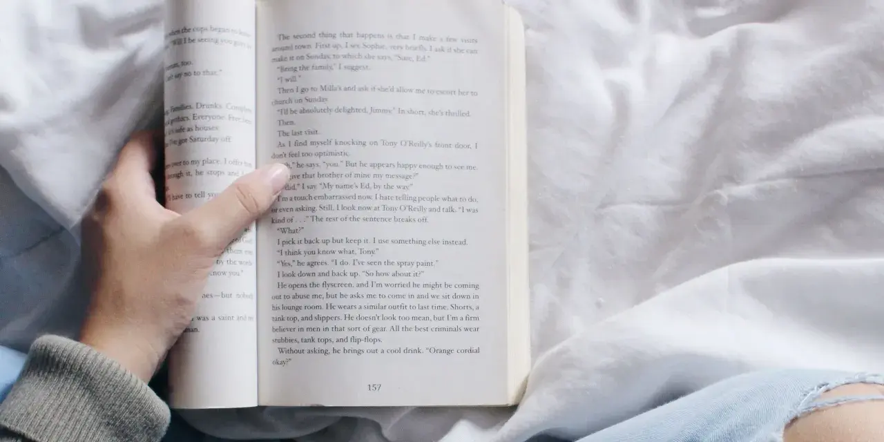 Mano sosteniendo un libro abierto con relatos cortos para mujeres. La página muestra texto y el número 157.