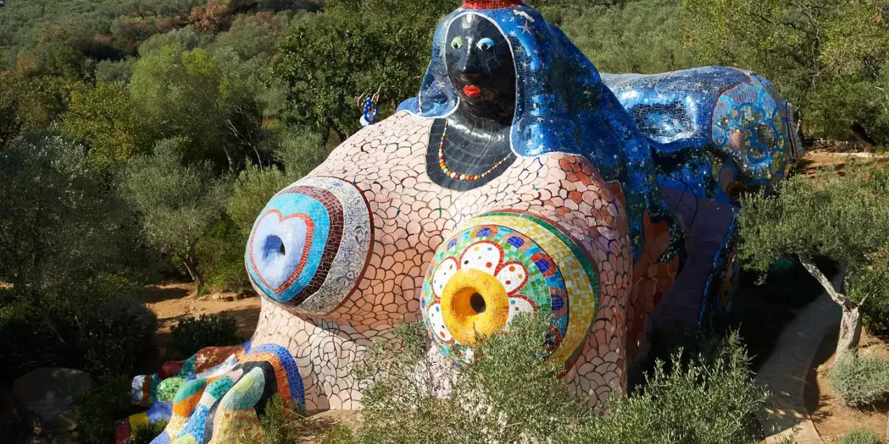 Œuvres d'art de Niki de Saint Phalle : une sculpture monumentale et colorée, représentant une femme allongée, ornée de mosaïques vives, dans un paysage verdoyant.