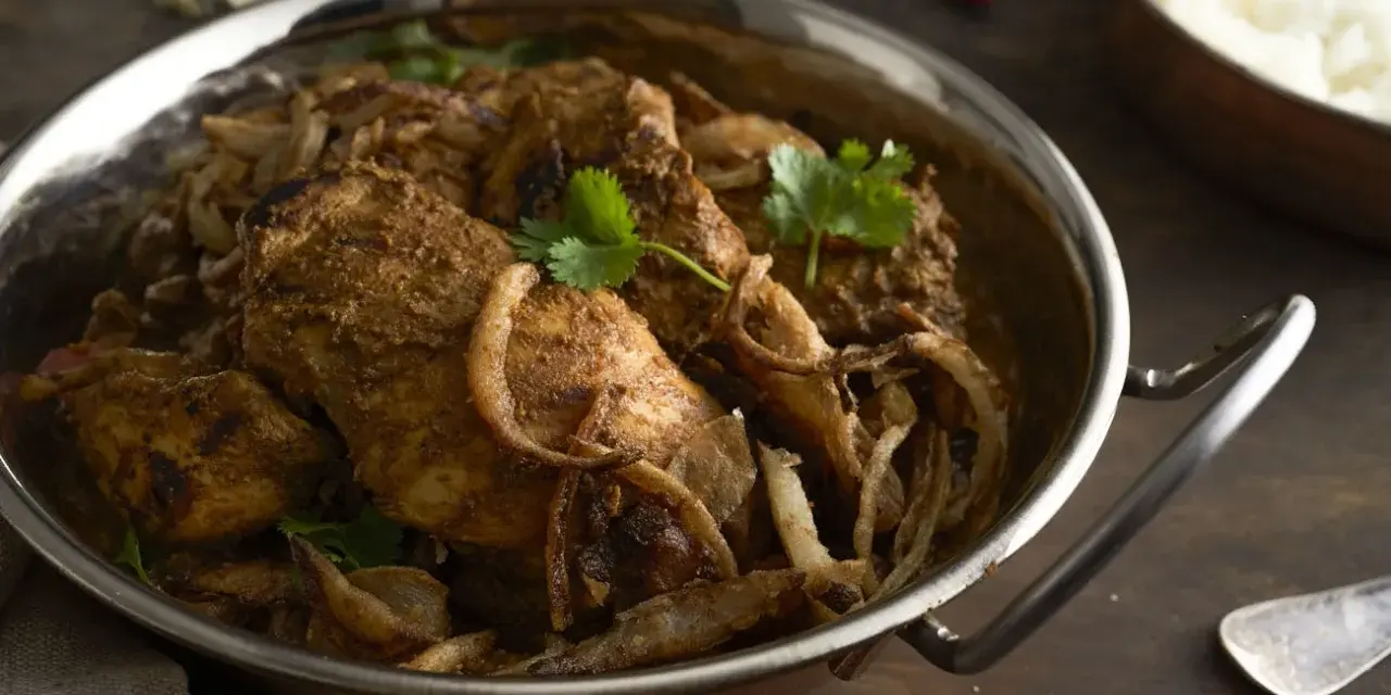 Kurczak w sosie garam masala z cebulą i kolendrą w metalowej misie.