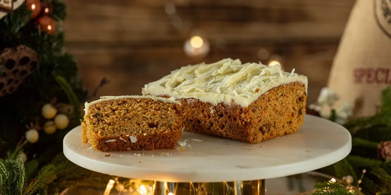 Pyszny, wilgotny naked cake marchewkowy z kremem i wiórkami białej czekolady, udekorowany świątecznymi światełkami i gałązkami choinki.