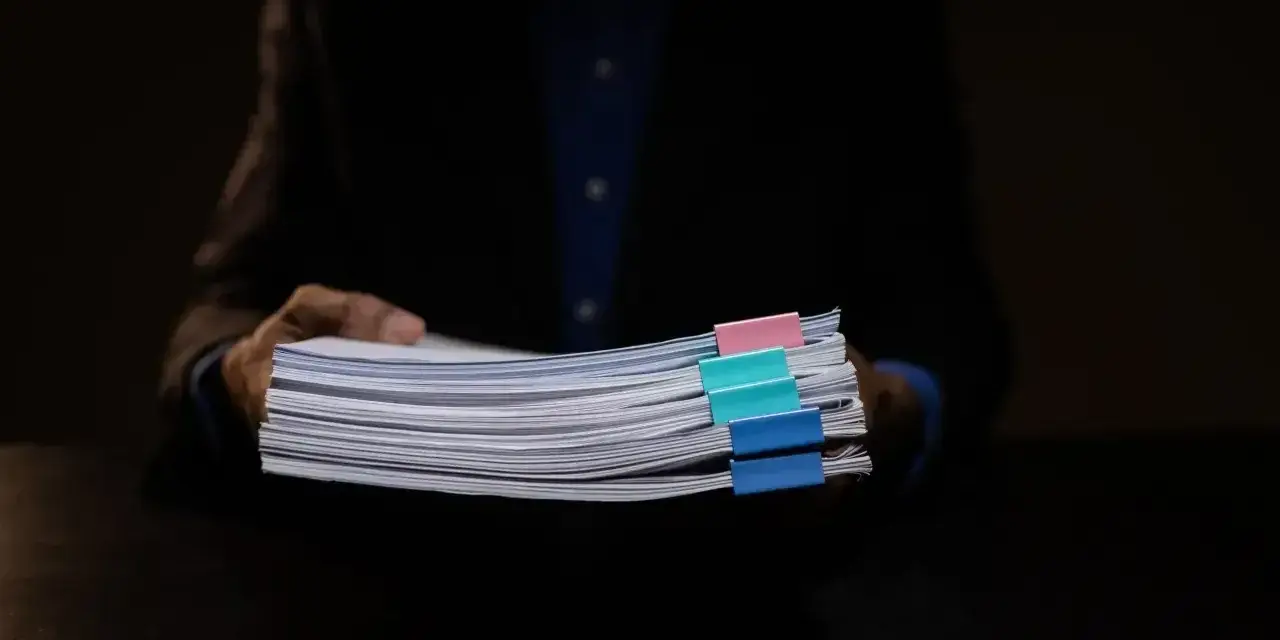 Mężczyzna w garniturze trzyma stos dokumentów z kolorowymi spinaczami. Może to być materiał dowodowy w sprawie hipoteka przymusowa.