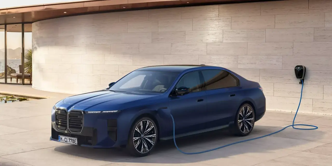Elegancka, granatowa BMW hybryda podłączona do ładowarki przy nowoczesnym domu z widokiem na morze.