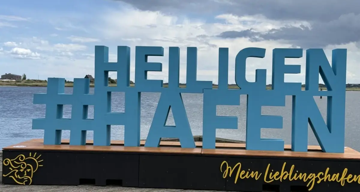 Große blaue Buchstaben mit #Heiligenhafen auf einem Holzpodest. Perfekt für Ausflugsziele und Erinnerungen an diesen schönen Ort.