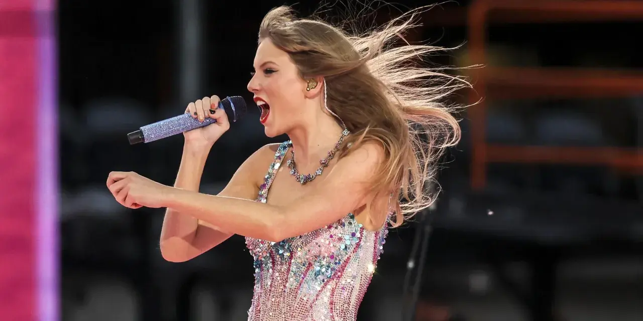 Taylor Swift w błyszczącej sukience śpiewa na koncercie w Warszawie, włosy rozwiane przez wiatr.