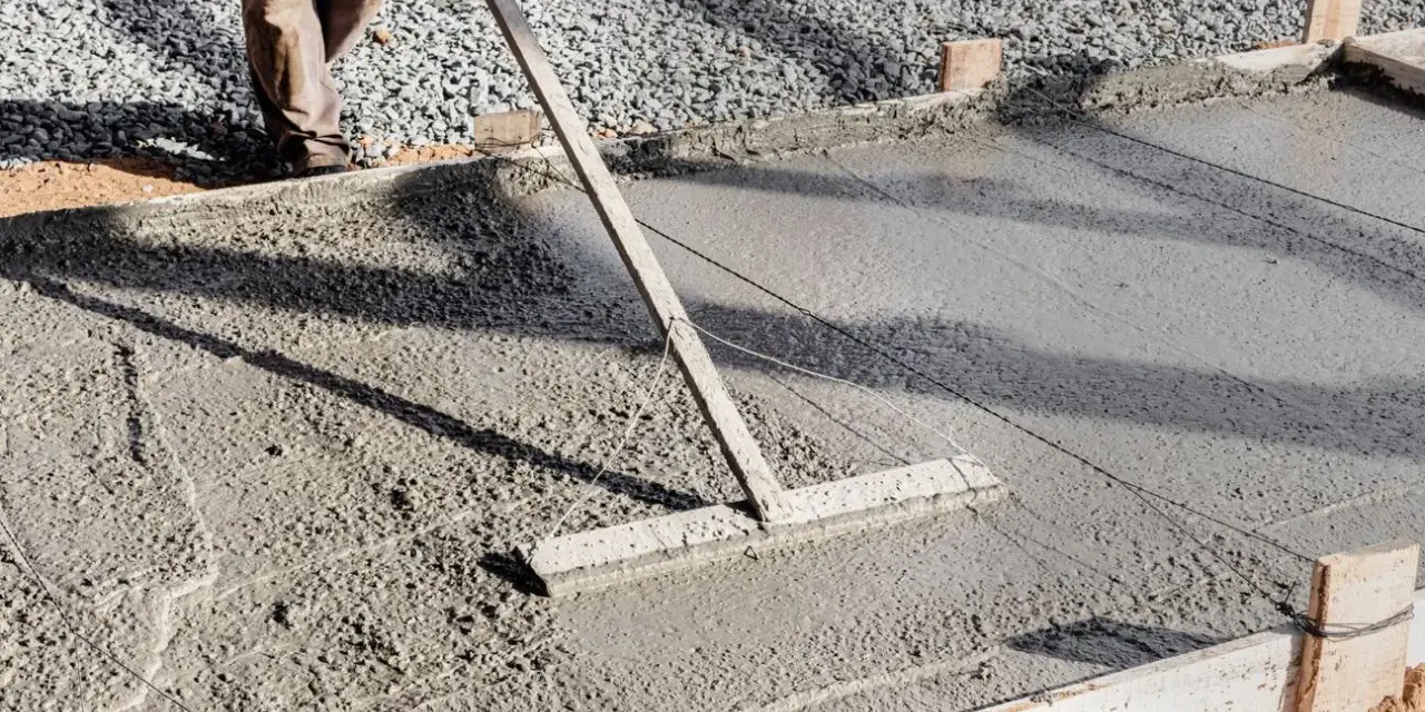 Un ouvrier utilise un râteau pour lisser du béton frais, étape essentielle pour faire une dalle béton solide.