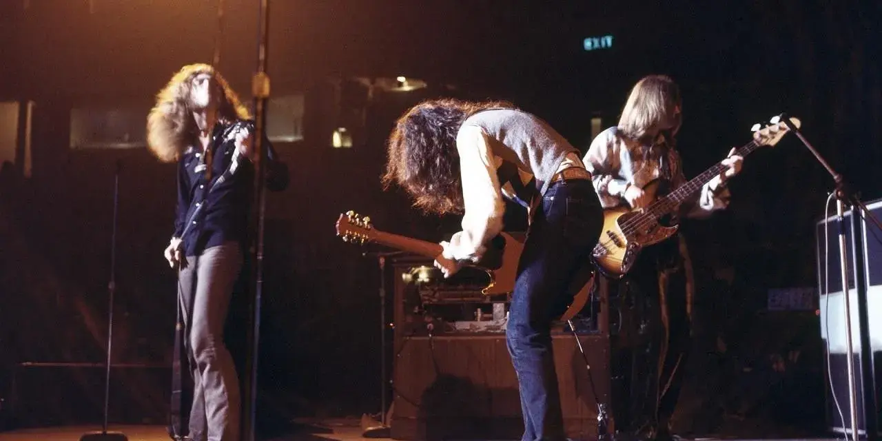 Energetyczny **Led Zeppelin koncert** na scenie. Wokalista z burzą włosów, gitarzysta pochylony nad instrumentem, basista grający w tle.