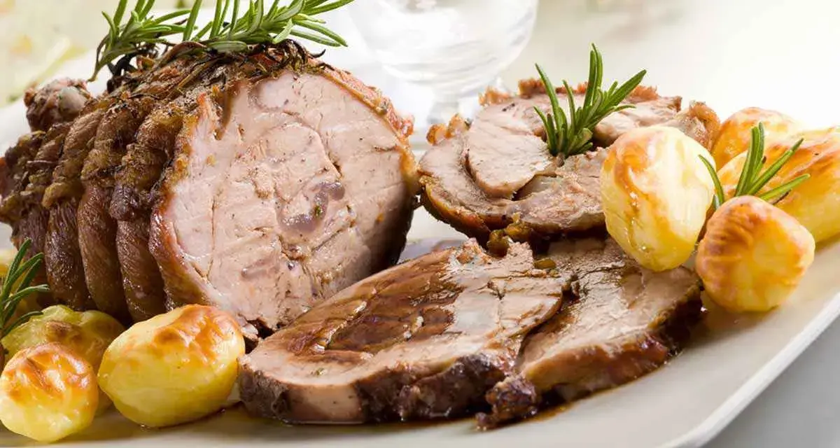 Succulento arrosto di vitello affettato, guarnito con rosmarino e accompagnato da patate arrosto dorate.