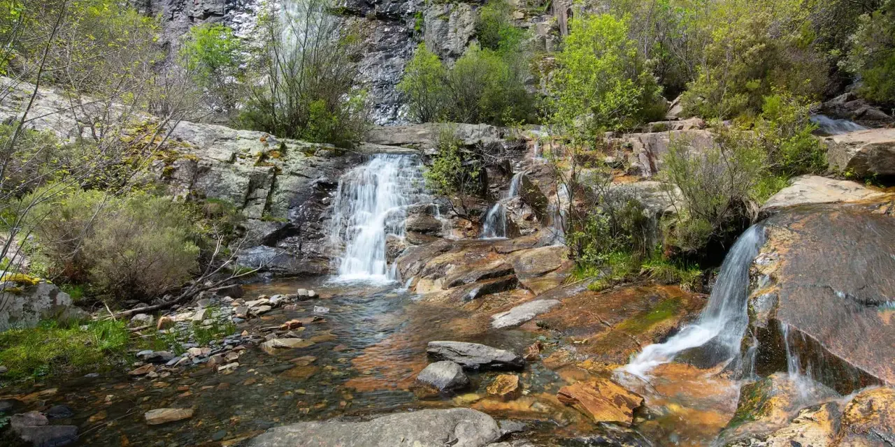 Las chorreras de despeñalagua, cascadas de agua blanca cayendo sobre rocas rojizas y verdes arbustos en un paisaje rocoso.