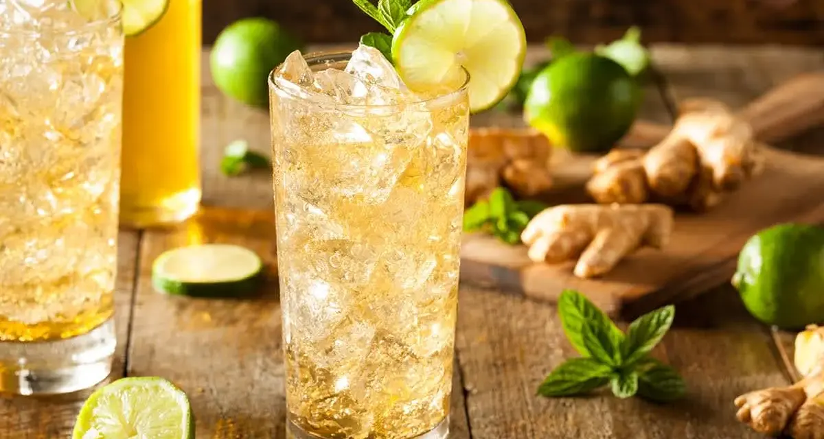 En uppfriskande ginger beer drink med is, lime och mynta. Ingredienser som ingefära och lime ligger utspridda.