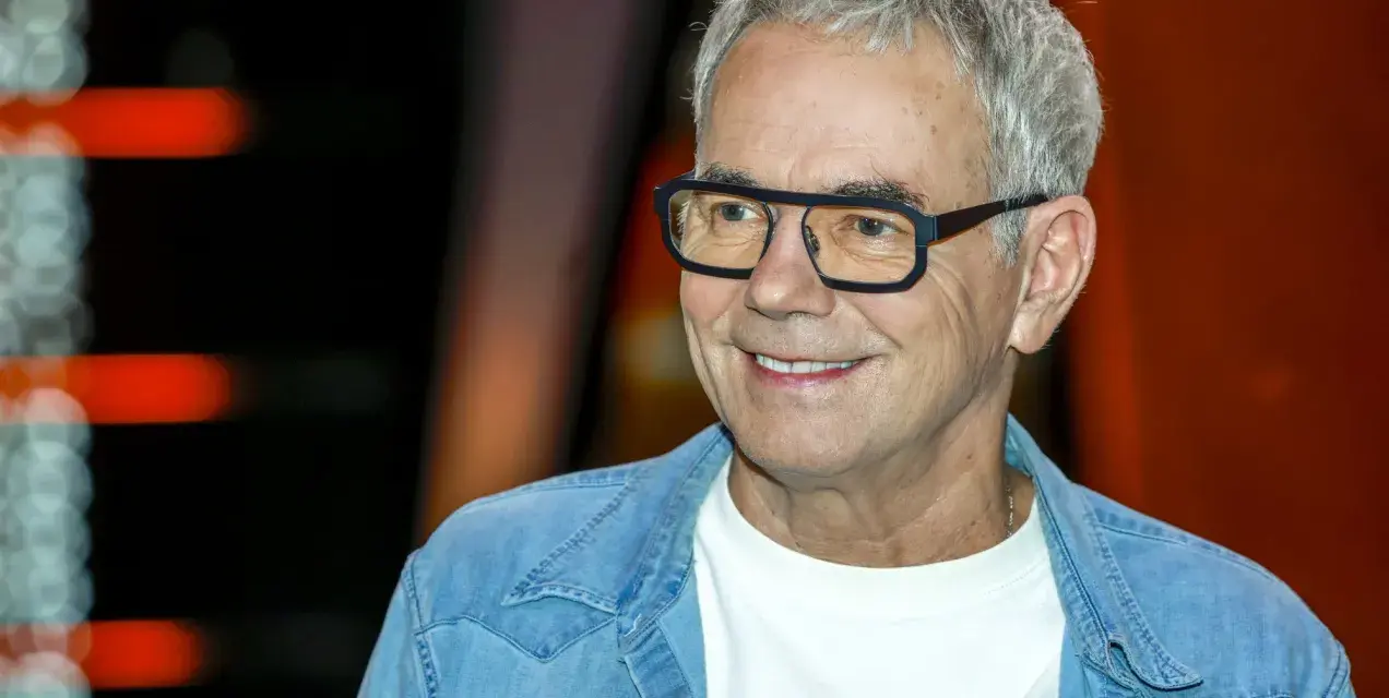 Uśmiechnięty mężczyzna w okularach, w jeansowej koszuli, jakby czekał na pytanie: "Jaka to melodia?".