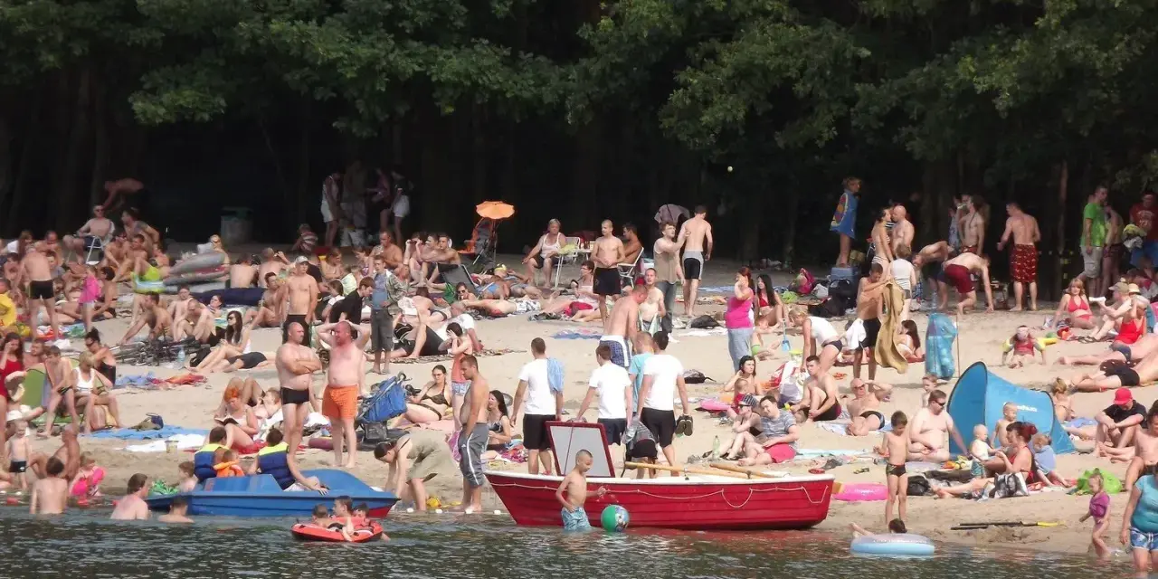 Tłum ludzi odpoczywa na plaży nad jeziorem w Jelczu Laskowicach. Słońce, piasek i woda tworzą idealne warunki do letniego relaksu.