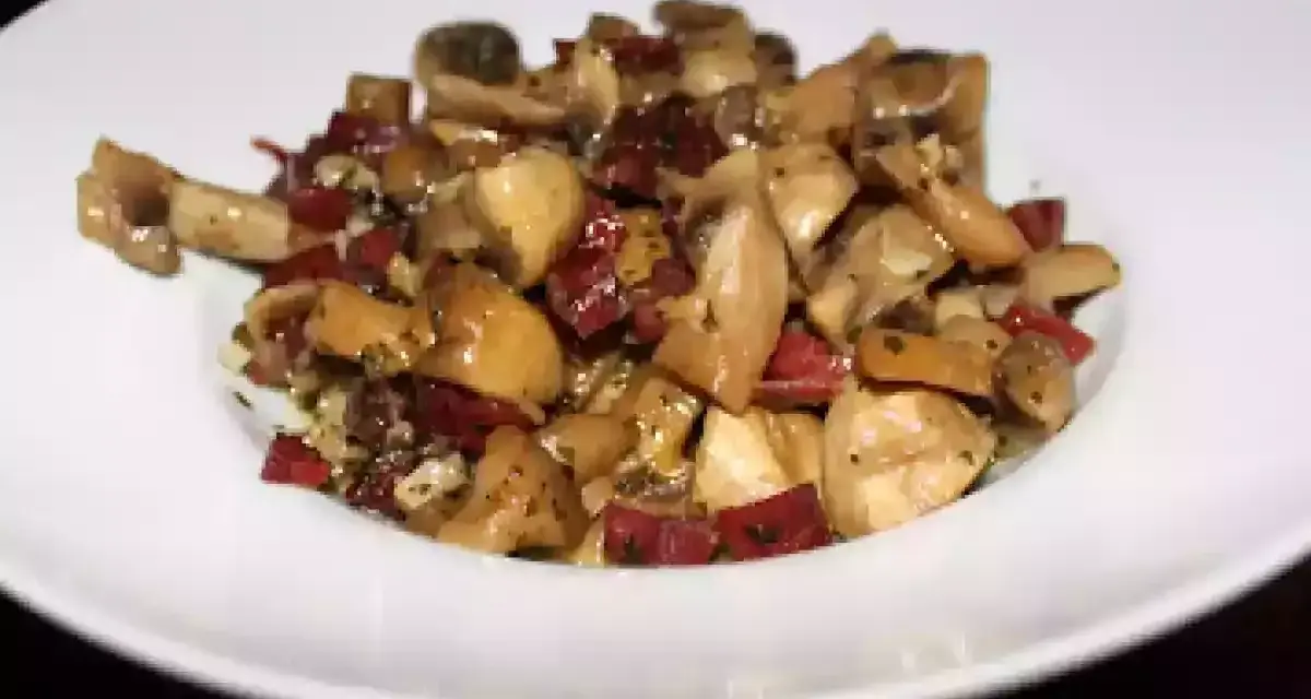 Champiñones salteados con trocitos de jamón, servidos en un plato blanco. Un plato sencillo y sabroso.