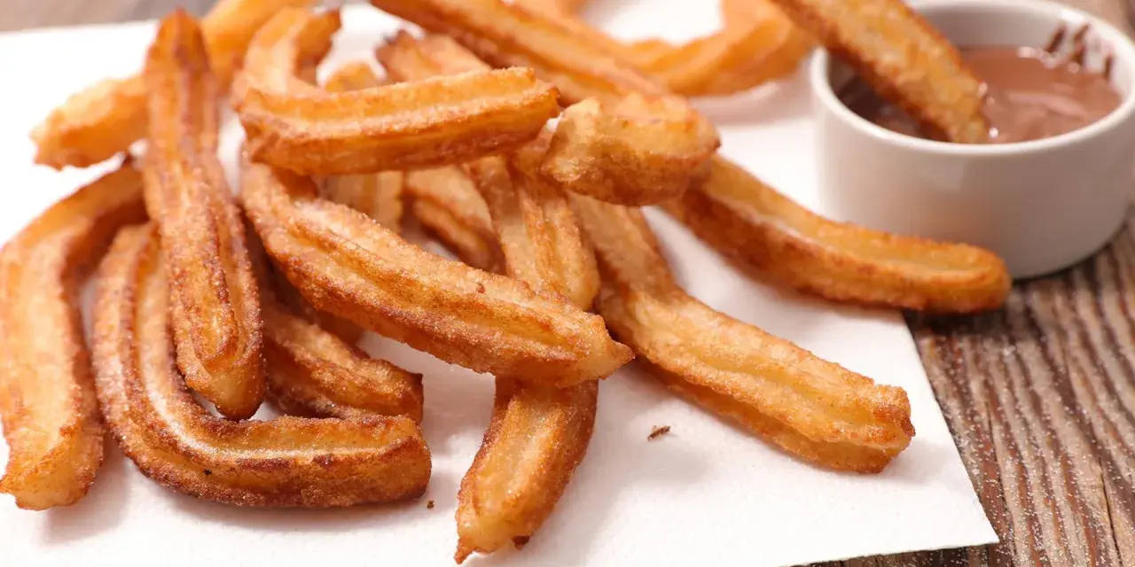 Goldbraune Churros, frisch frittiert, mit Zucker bestreut. Ein Churro wird in eine Schüssel mit Schokoladensauce getunkt. Ein echtes Churros Rezept Original.