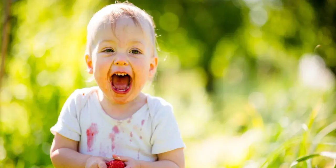 Uśmiechnięte 1.5 roczne dziecko nie mówi mama, ale z radością trzyma truskawkę.