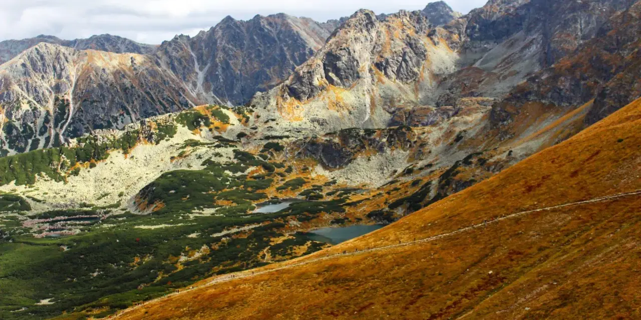 Widok na Tatry jesienią. Widać szlak turystyczny, którym idzie się na Kasprowy, małe stawy i skaliste szczyty.