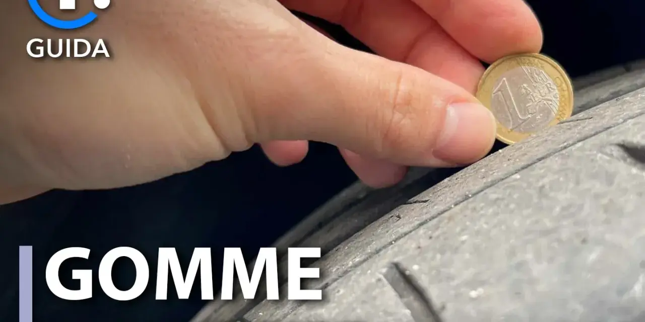 Una mano tiene una moneta da 1 euro per controllare l'usura di una gomma. Gomme lisce come capire quando cambiarle.