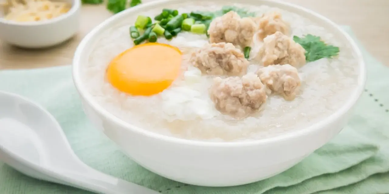Miseczka pysznego congee z mięsnymi klopsikami, jajkiem i szczypiorkiem. Idealne na rozgrzewający posiłek.
