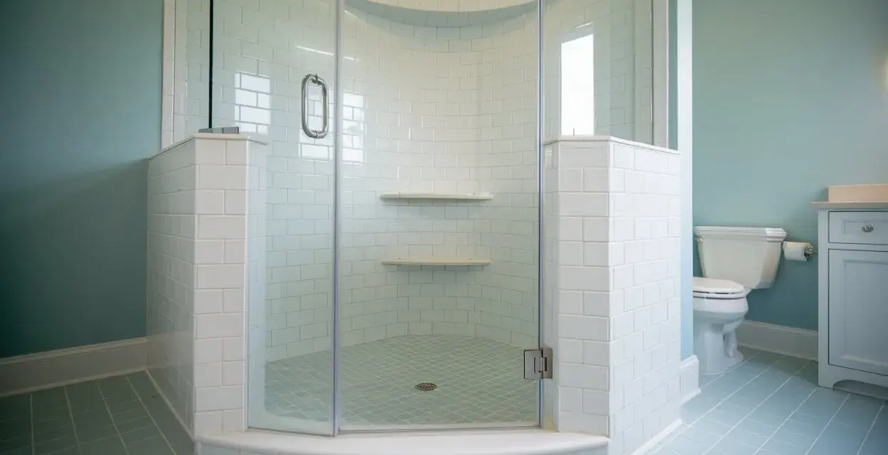 Salle de bain avec carrelage bleu pâle et une douche d'angle. Ce receveur de douche à éviter, avec ses étagères peu pratiques, est un cauchemar à nettoyer.