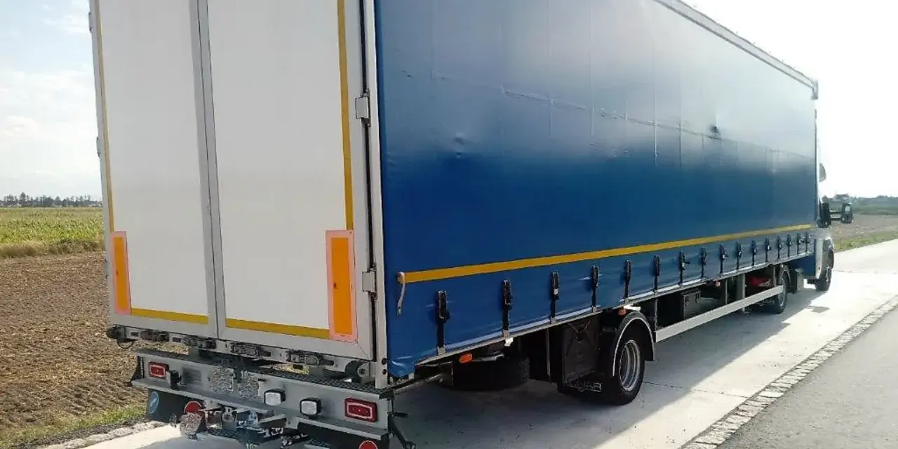 Tylna część niebieskiej naczepy z białymi drzwiami, stojąca na poboczu. To część zespołu pojazdów gotowego do drogi.