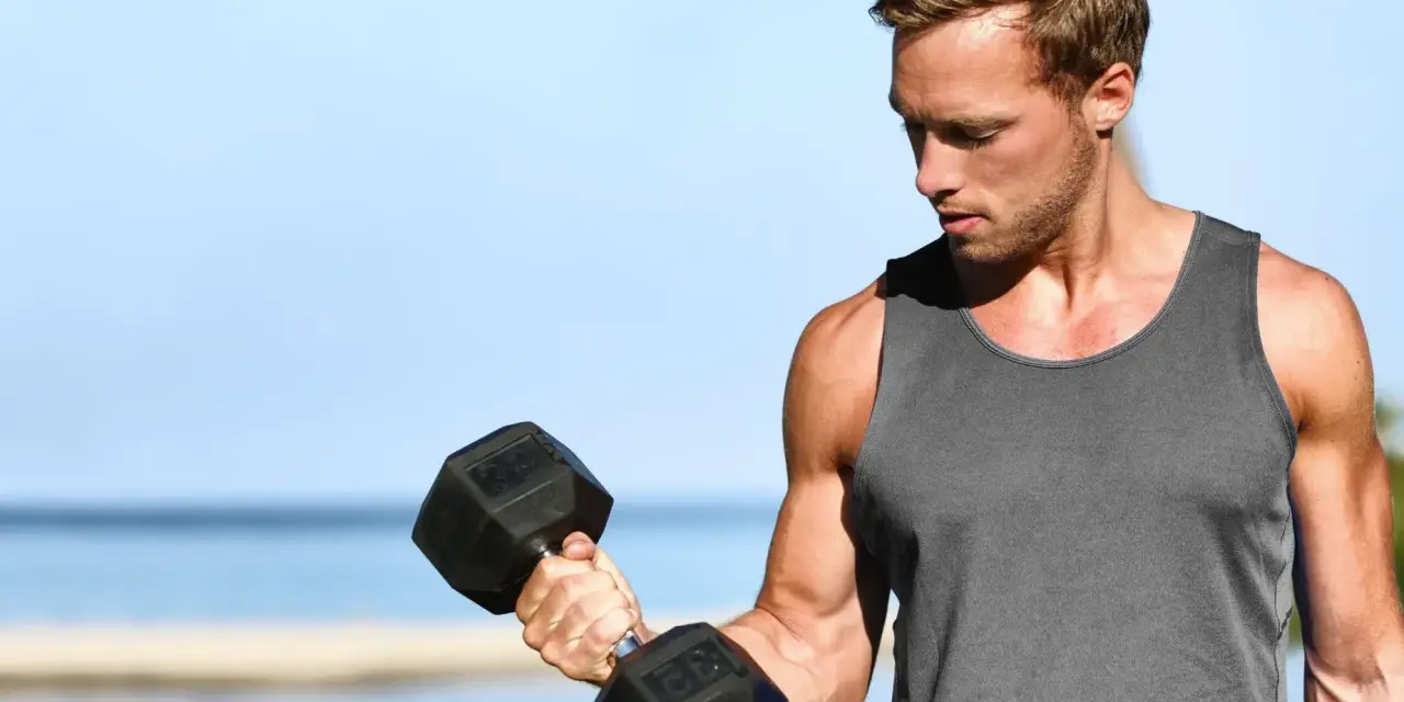 Mężczyzna ćwiczy biceps na plaży, zastanawiając się, ile serii na biceps w tygodniu da najlepsze efekty.