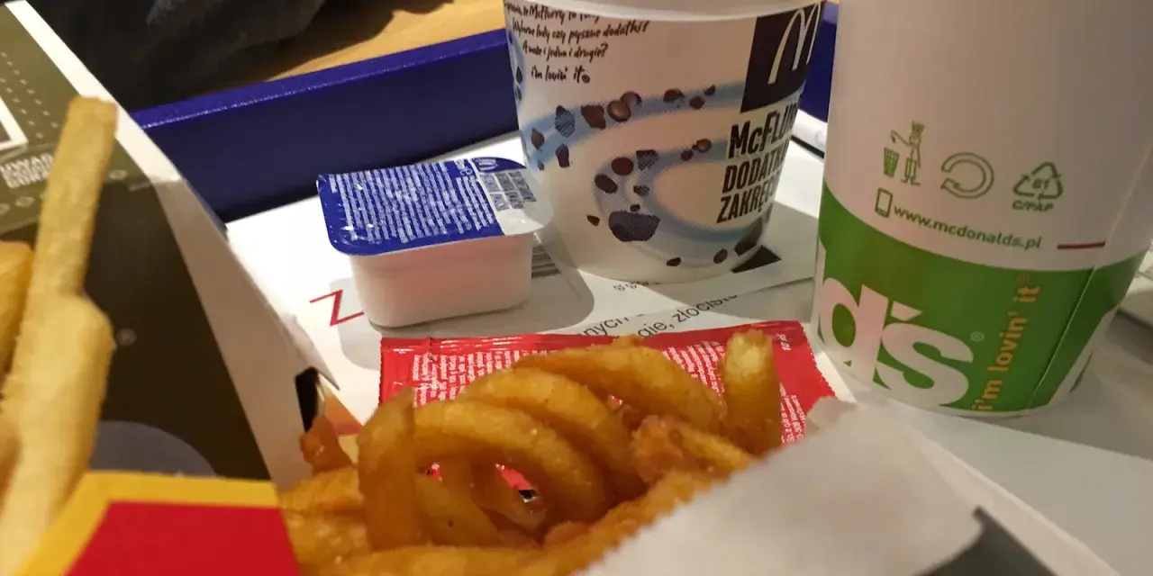 Zakręcone frytki McDonald's w pudełku z sosem i napojem.