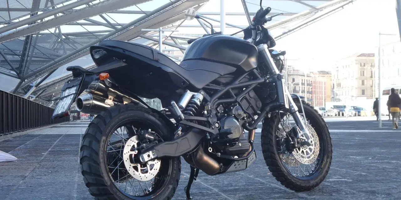 La Moto Morini Scrambler 1200, nera e imponente, si staglia sotto una struttura metallica moderna.