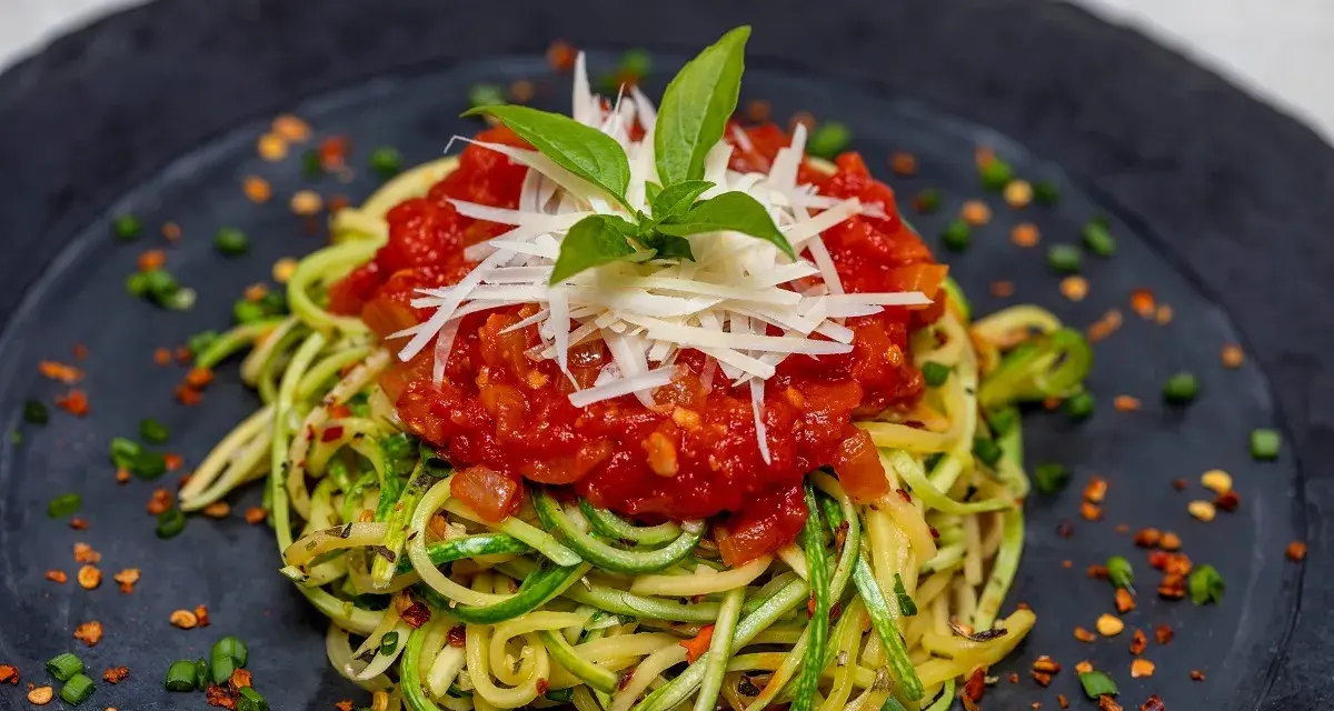 Deliciosa pasta con verduras, hecha de calabacín en espiral, cubierta con salsa de tomate y queso rallado.