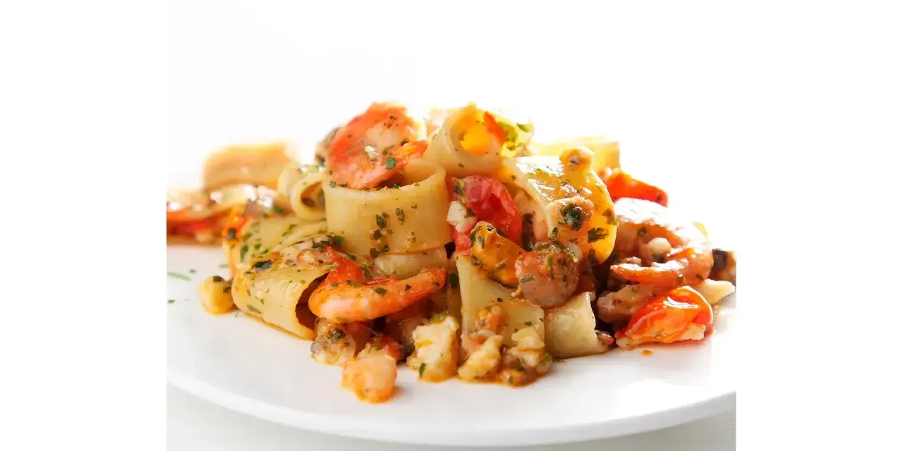 Piatto di calamarata allo scoglio con gamberi, cozze e pomodorini, condita con prezzemolo fresco.