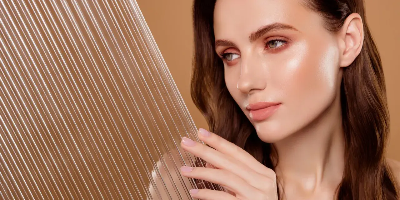 Kobieta z idealną cerą, która emanuje blaskiem, niczym efekt glass skin. Delikatne linie na pierwszym planie dodają głębi.