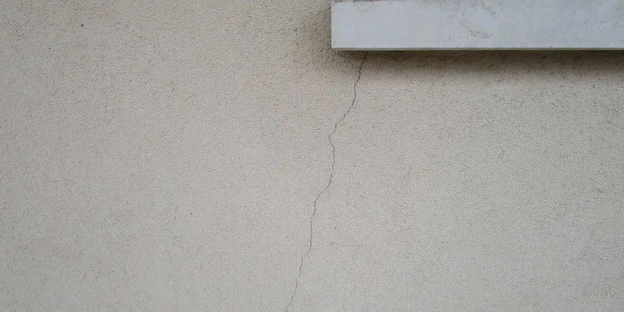 Crepa sottile su muro esterno, vicino a davanzale e inferriata. Necessaria riparazione crepe strutturali.