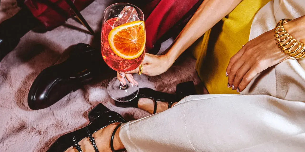 Elegancka kobieta z drinkiem, zastanawia się: martini co to? Złota biżuteria i czarne buty dodają szyku.