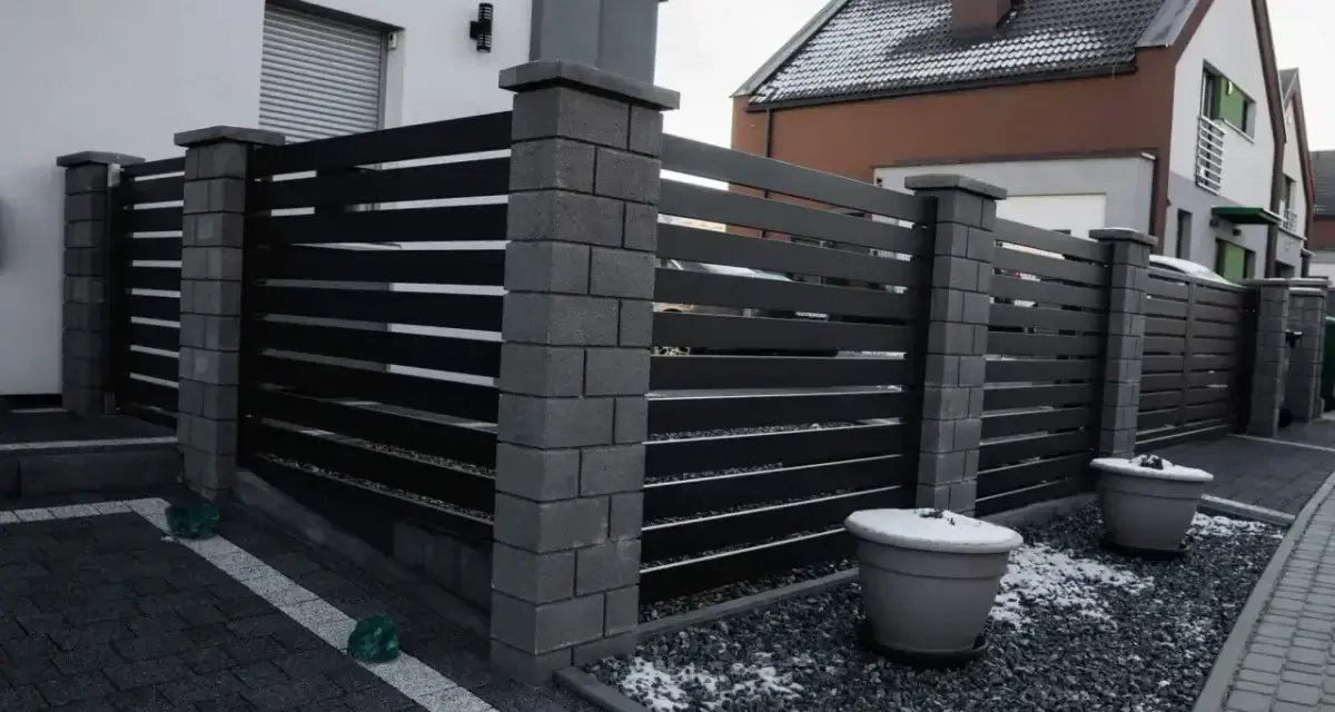 Nowoczesne ogrodzenie z betonowych słupków i ciemnych paneli. Taka wysokość ogrodzenia bez pozwolenia zapewnia prywatność.