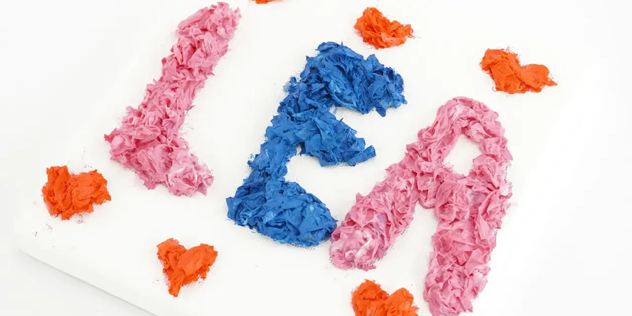 Comment faire du relief sur un tableau : des lettres "LÉA" en papier froissé rose et bleu, entourées de cœurs orange sur une toile blanche.