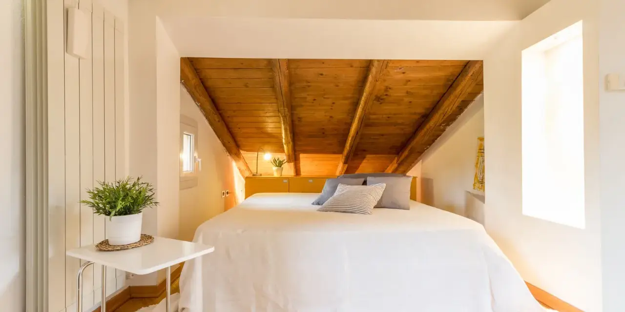 Accogliente camera da letto in mansarda con travi a vista in legno. Idee per un nido romantico e funzionale.